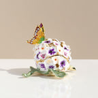 White and purple floral trinket box with butterfly on a light surface