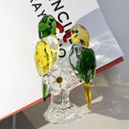 Green and yellow parrot pair on a clear base beside a book