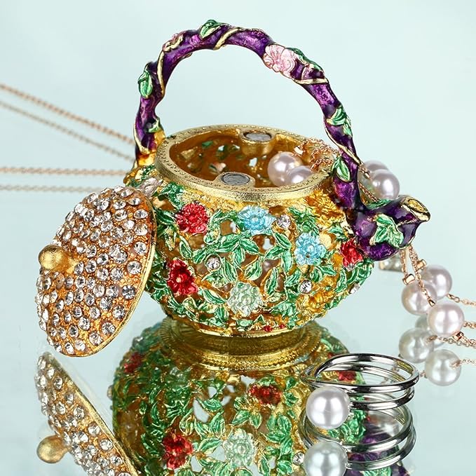 Open floral teapot trinket box beside rings and a pearl necklace
