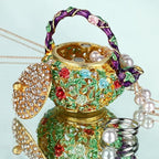 Open floral teapot trinket box beside rings and a pearl necklace
