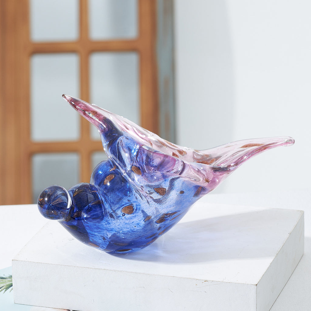 Glass conch shell sculpture displayed on a white block near a window