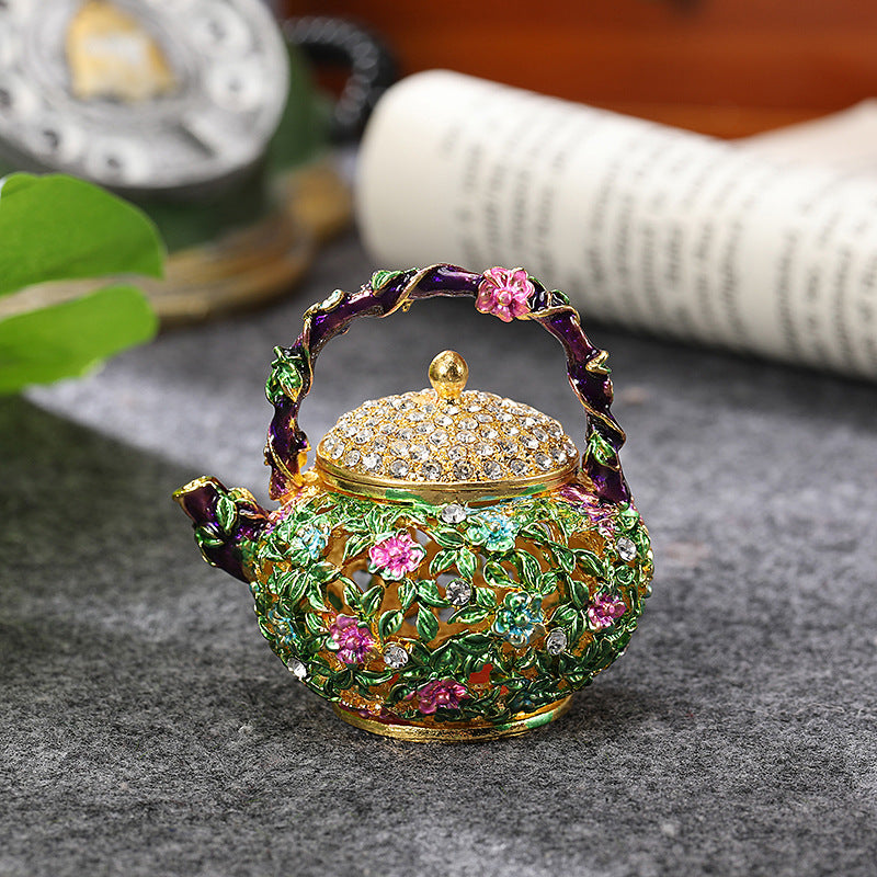 Floral teapot trinket box displayed on a gray surface beside a book