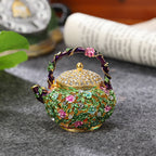 Floral teapot trinket box displayed on a gray surface beside a book