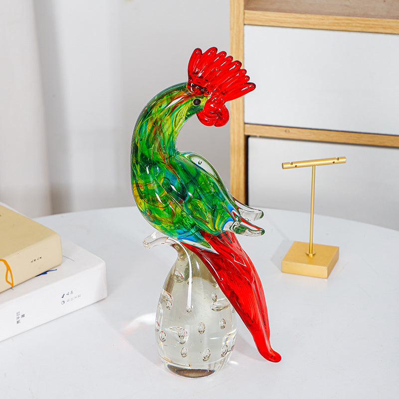 Green and red glass rooster figurine beside books on a white table